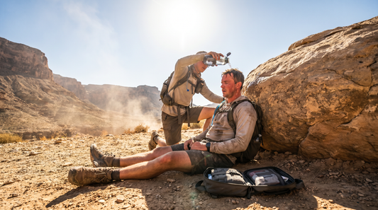 Wilderness first responder pouring water on a collapsed hiker in extreme desert heat with a PrepEM Wild medical kit open on the ground - heat stroke field guide 